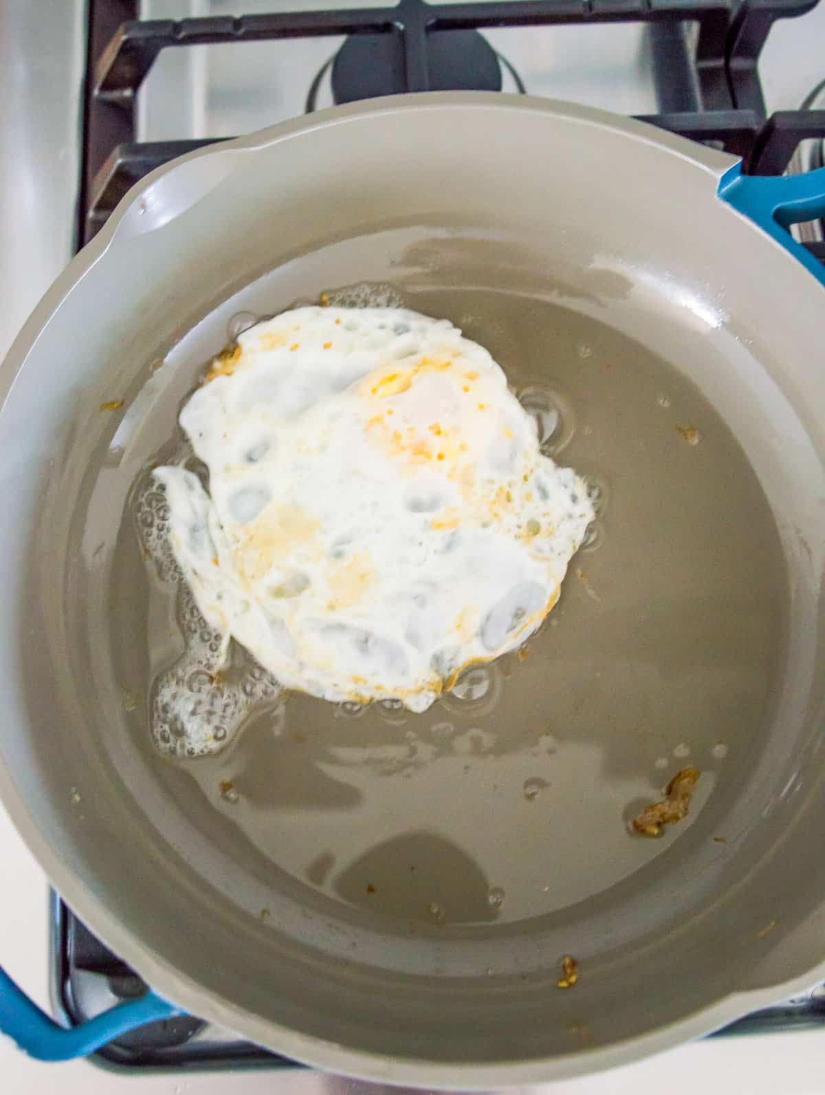 An over medium egg being cooked in a frying pan.