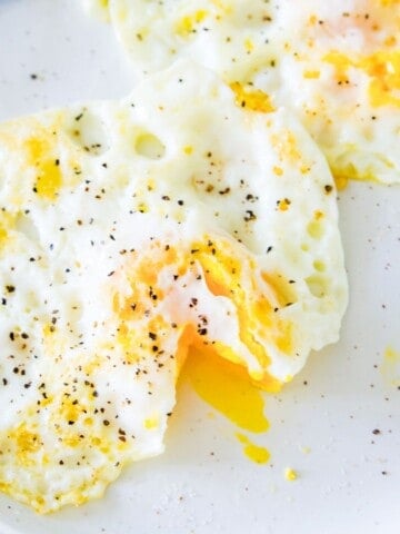 Two over medium eggs on a plate and one of them has the yolk cut open.