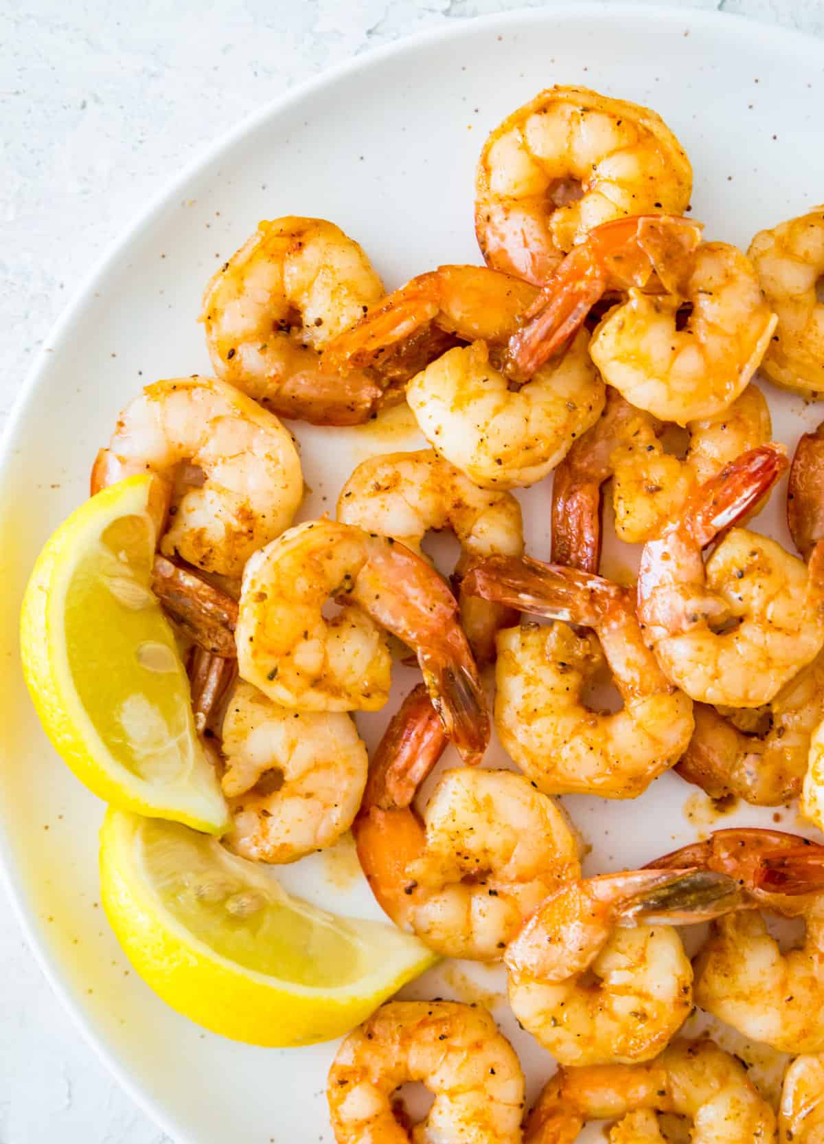 A plate with pan seared shrimp on it with lemon wedges beside them.