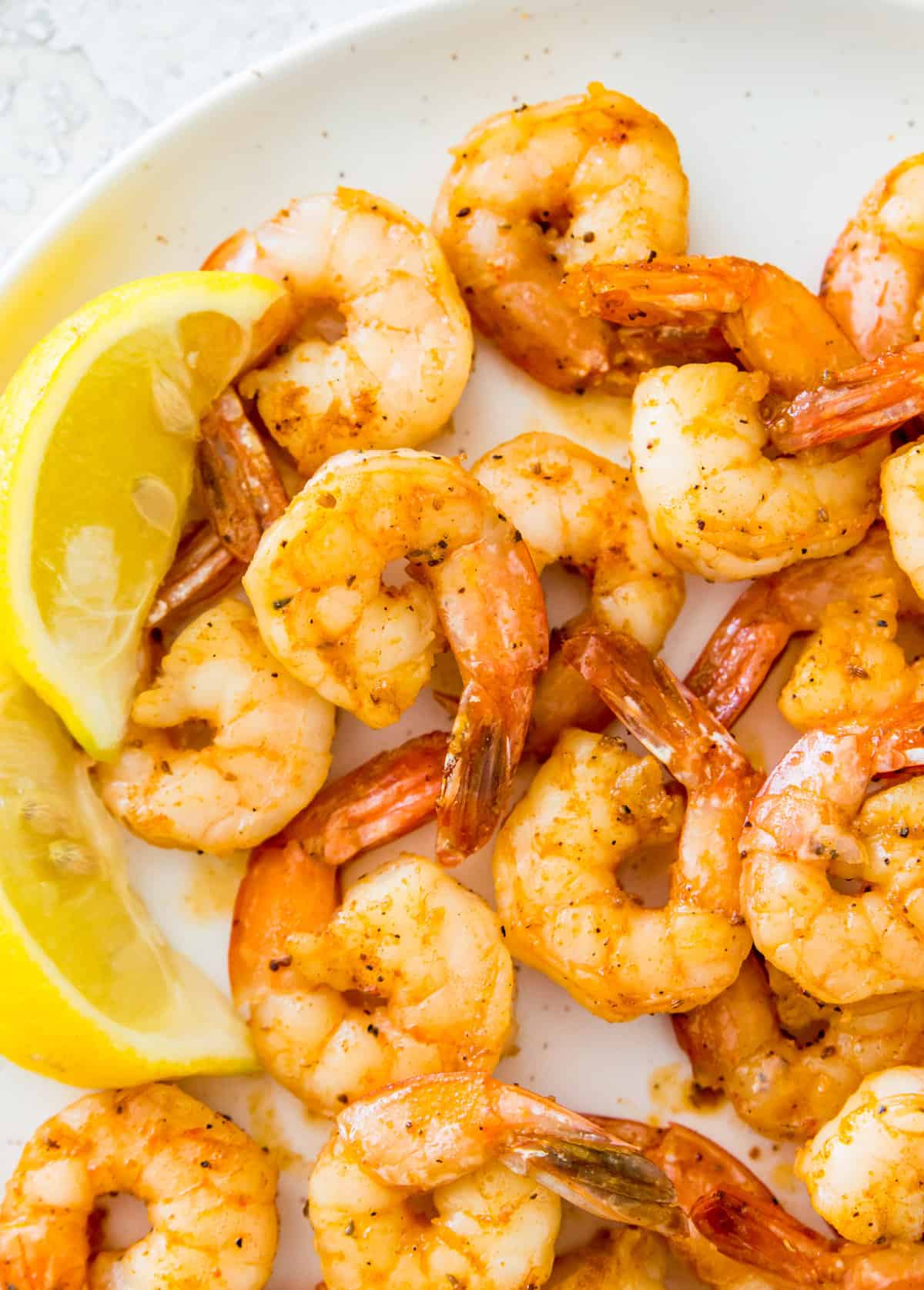 A plate of cooked shrimp with lemon wedges beside them.