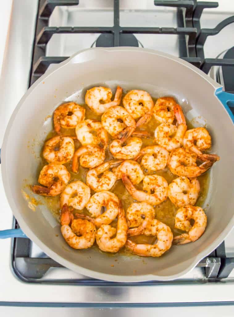 A pan with shrimp cooking in it on the stovetop.