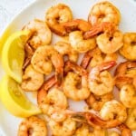 A plate with pan seared shrimp on it with lemon wedges around them.