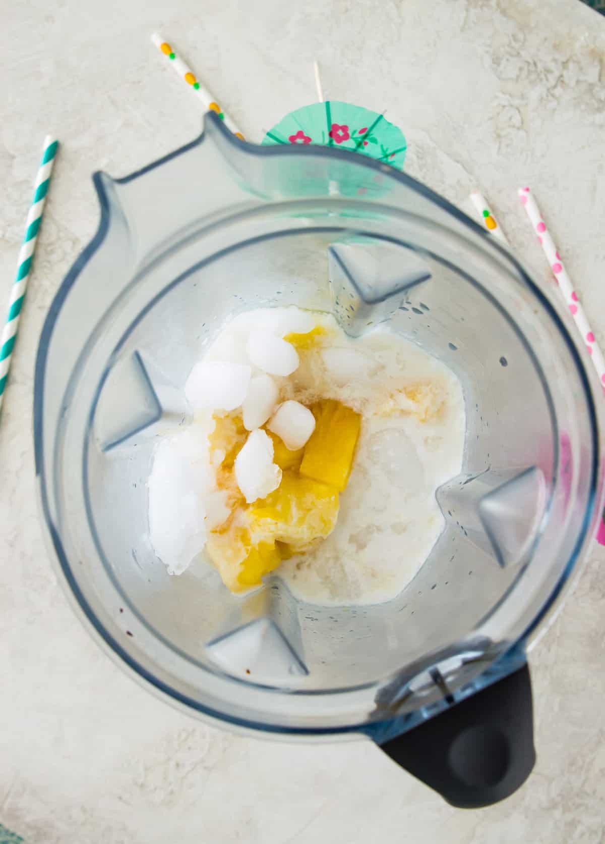 A blender filled with coconut milk, frozen pineapple chunks, ice and pineapple juice. 