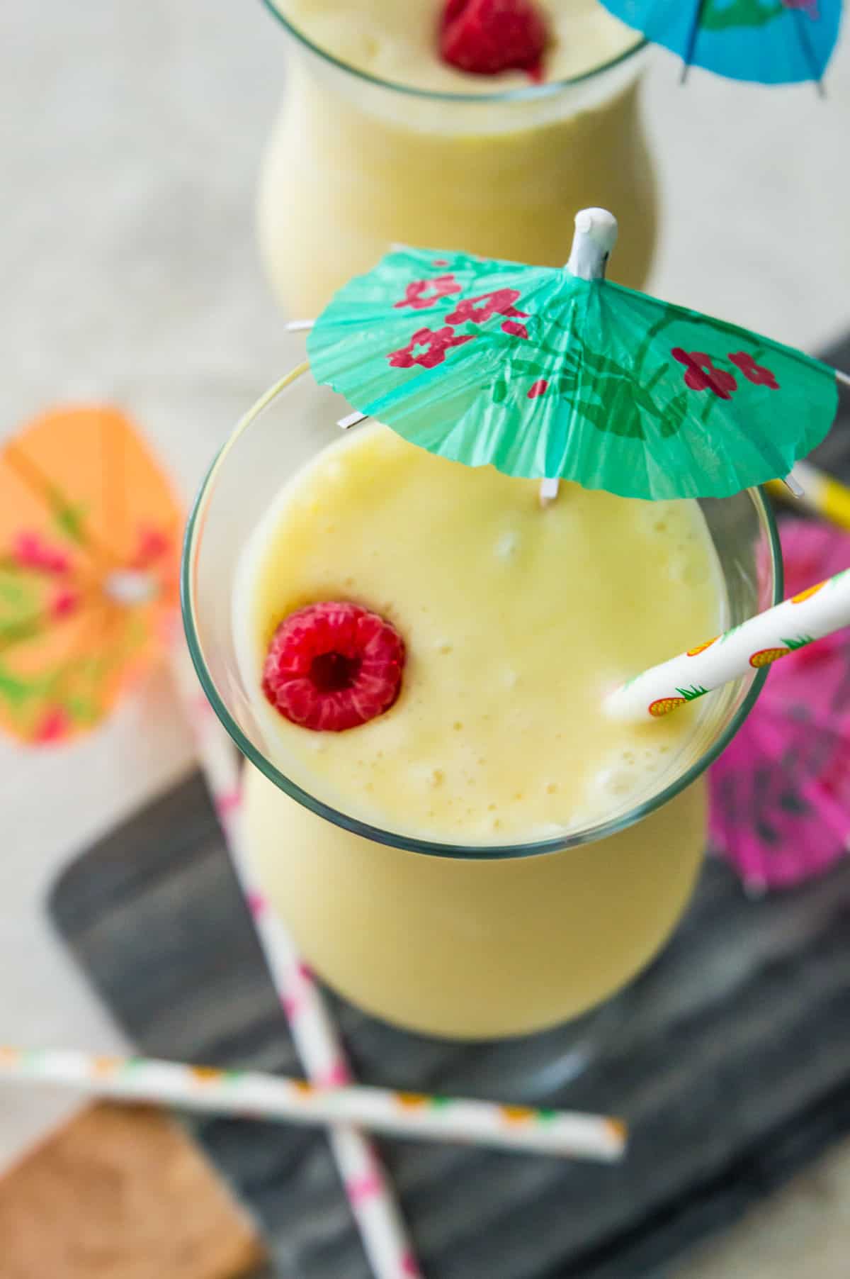 A glass of a piña colada mocktail topped with a fresh raspberry and a drink umbrella. 