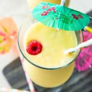 A piña colada mocktail topped with a green umbrella and a fresh raspberry. 