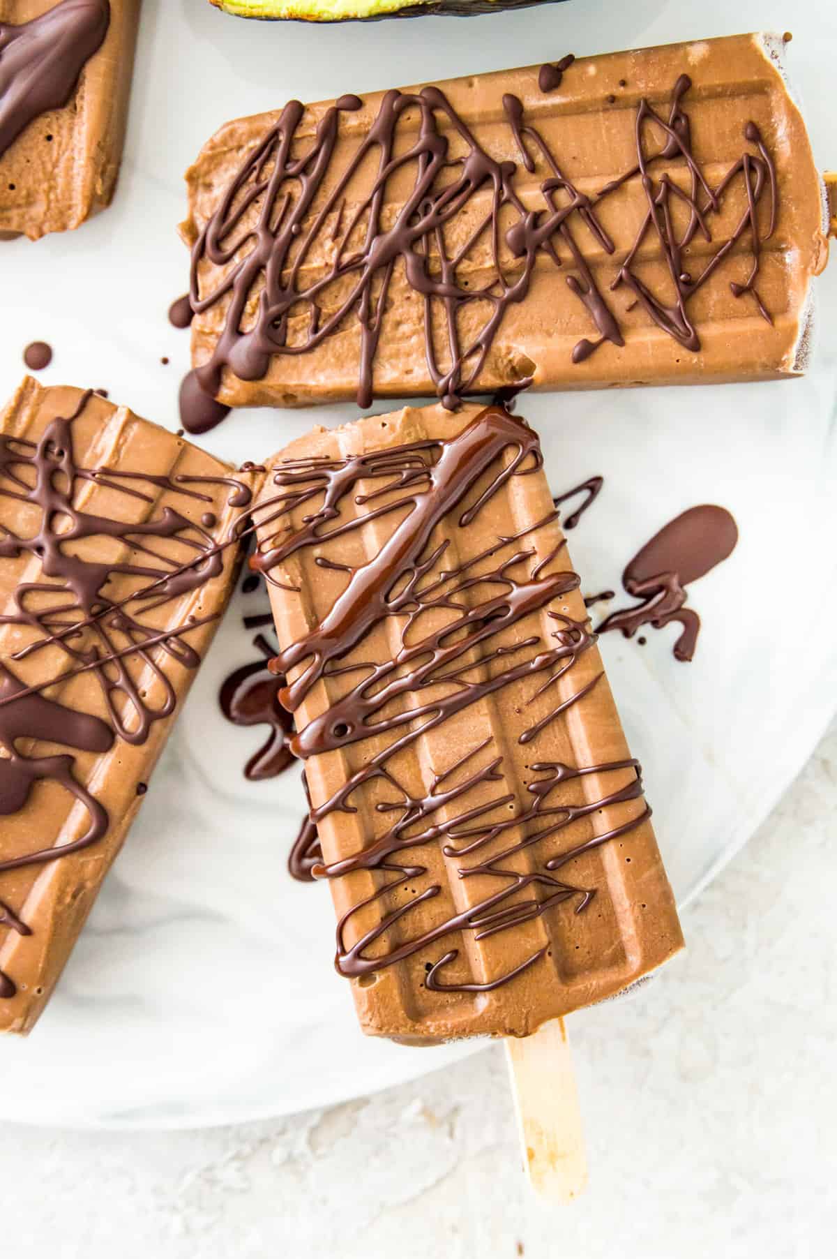 Avocado fudgesicles drizzled in melted chocolate on a serving tray.