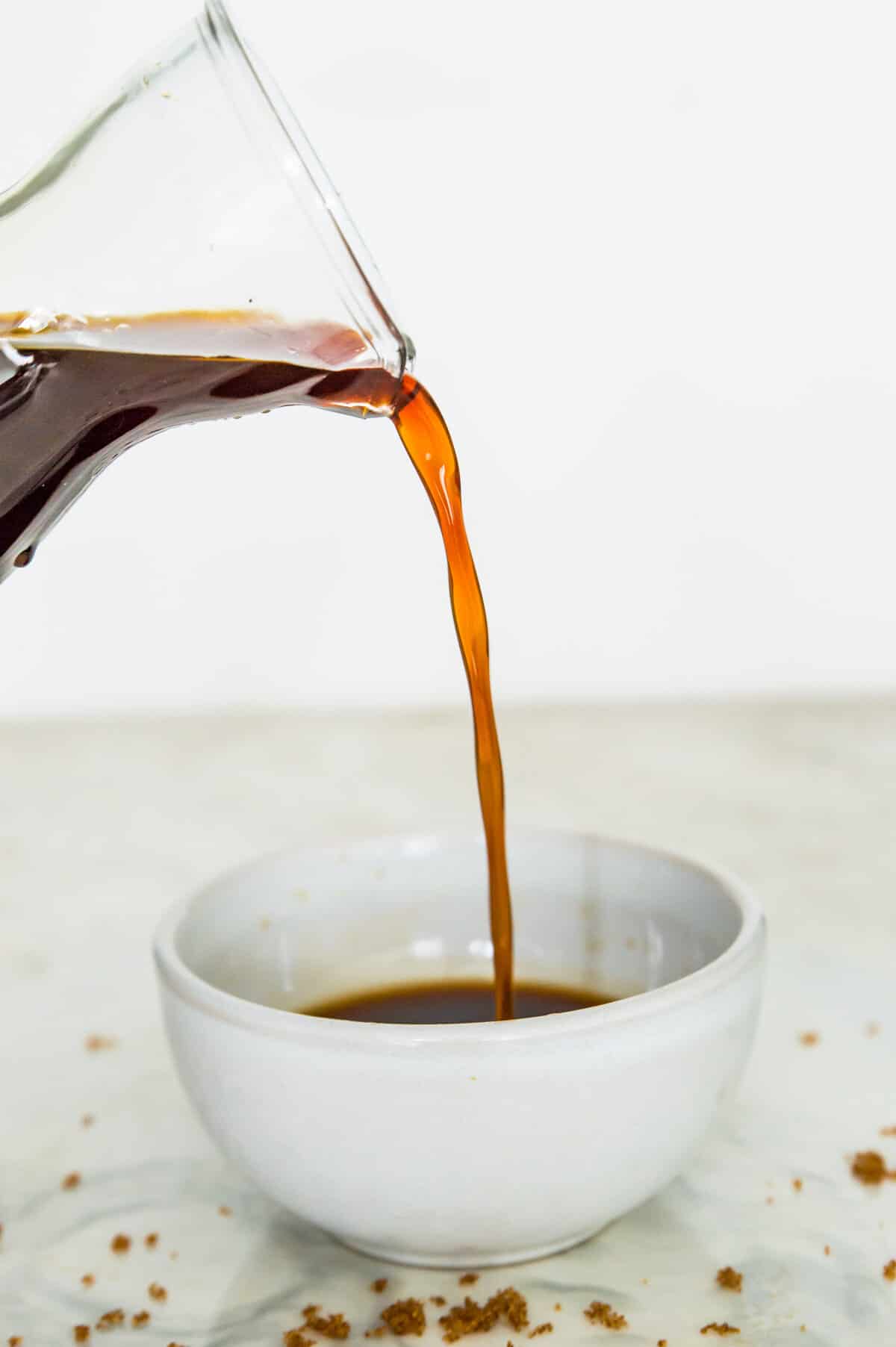 Brown sugar simple syrup being poured out of a glass bottle into a small bowl.