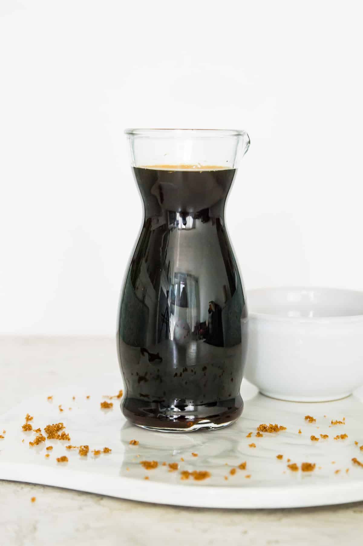 A glass bottle filled with brown sugar syrup with a white bowl next to it.