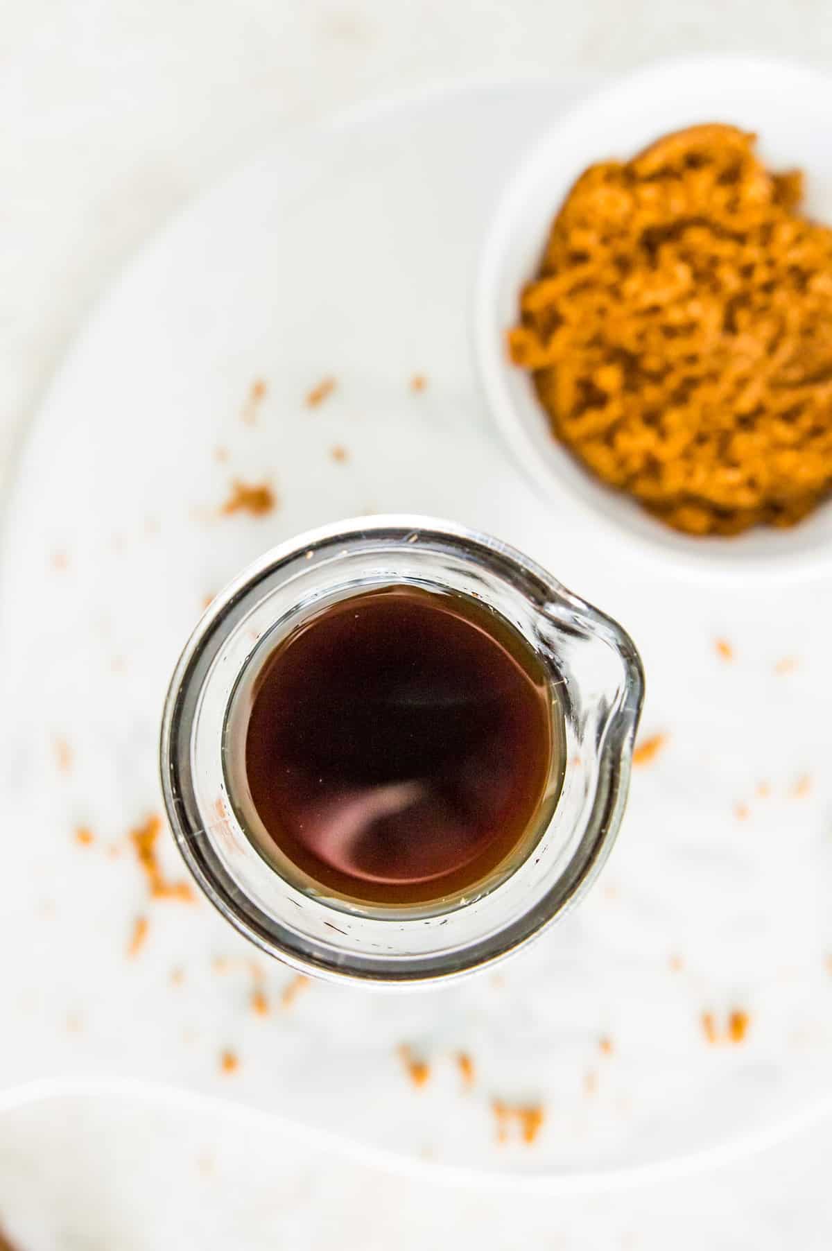 A glass bottle full of brown sugar simple syrup with a bowl of brown sugar next to it.