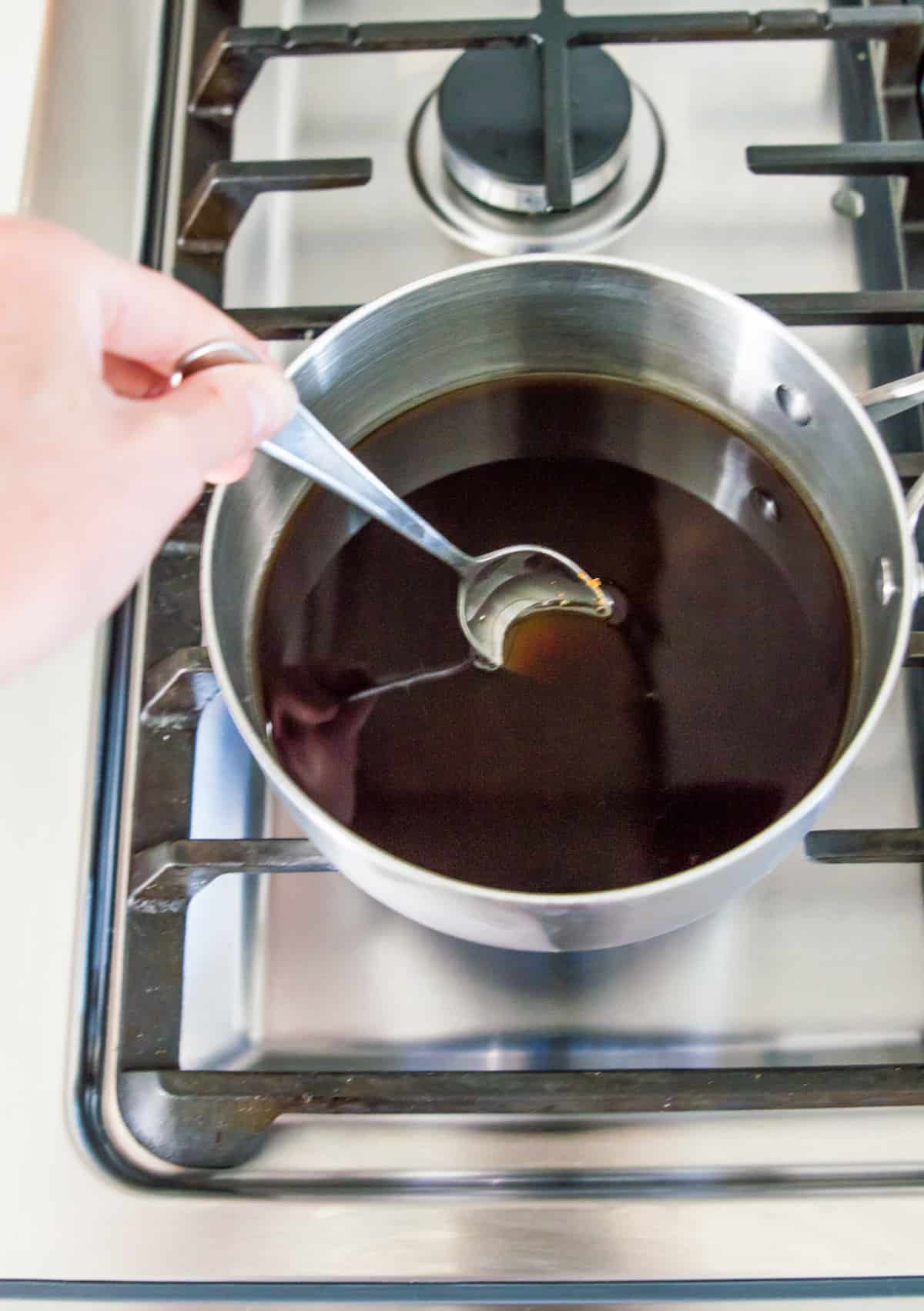 Brown sugar and water in a pot on the stovetop with a spoon stirring the mixture.