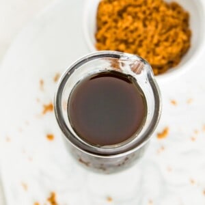 A glass bottle full of brown sugar simple syrup with a bowl of brown sugar next to it.