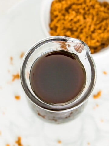 A glass bottle full of brown sugar simple syrup with a bowl of brown sugar next to it.