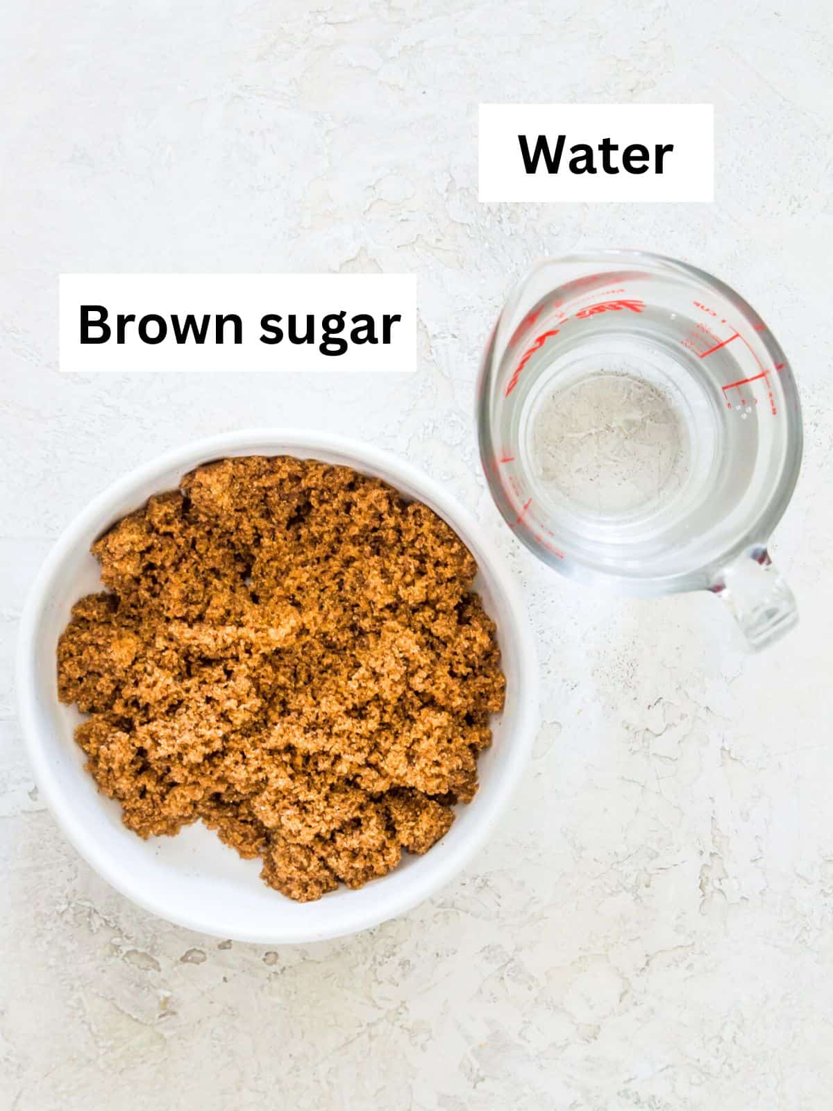 A white bowl filled with brown sugar and a glass measuring cup filled with water.