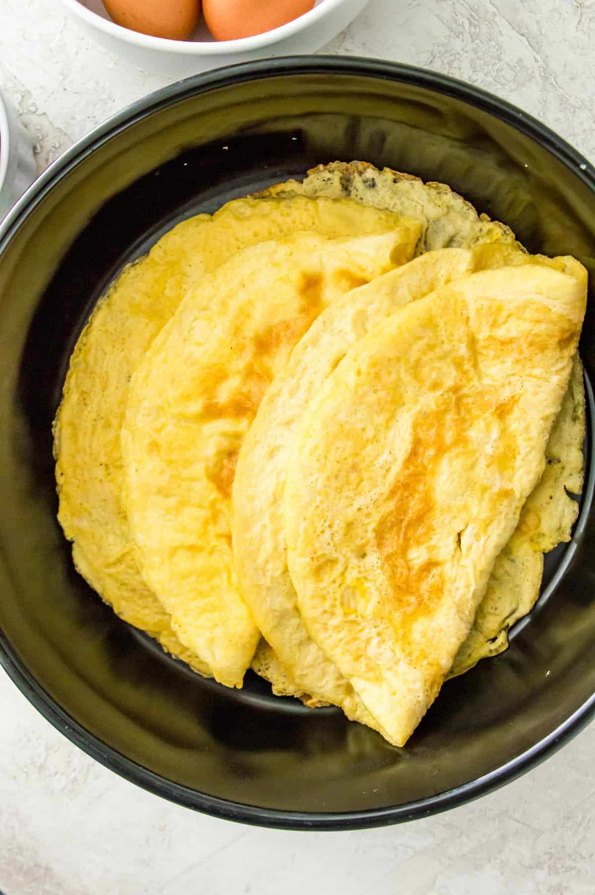 Egg wraps folded in half in a black frying pan.