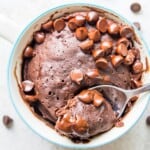 A chocolate gluten free mug cake topped with chocolate chips and with a spoon in it.