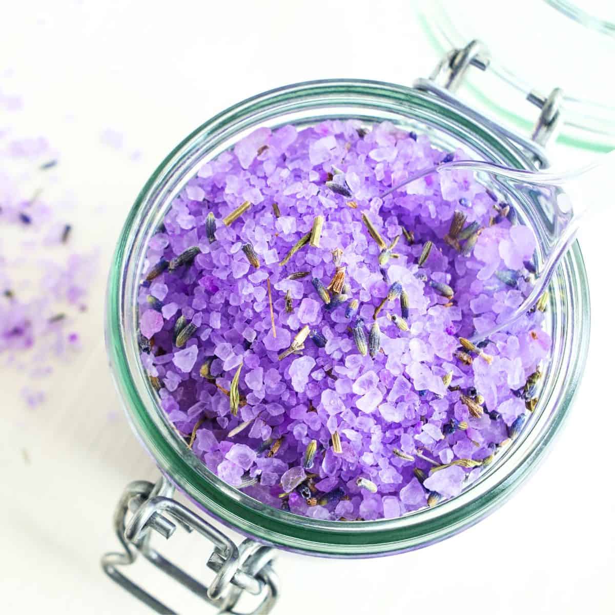 A jar full of lavender bath salts with a scoop in it.