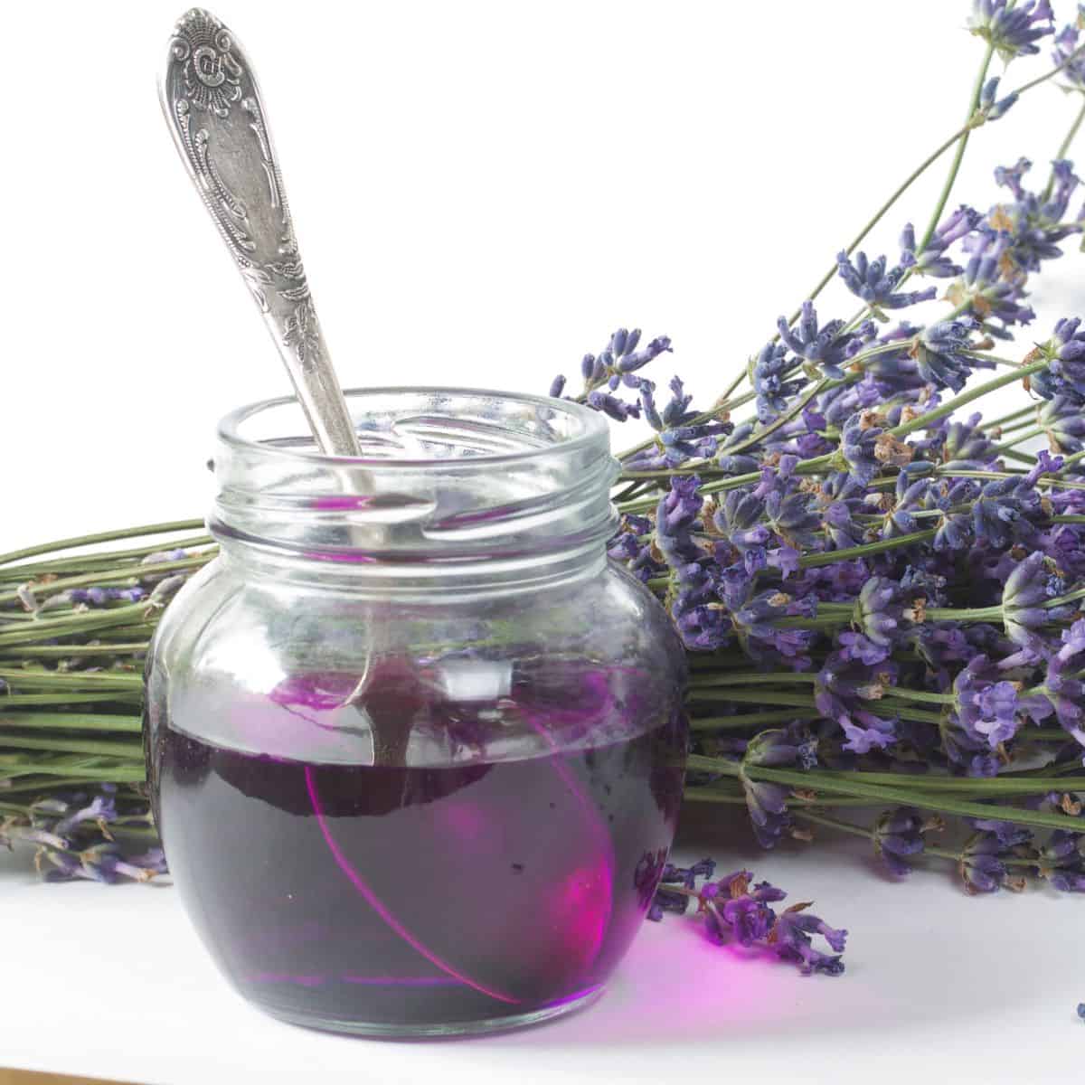 A jar of lavender simple syrup with a spoon in it.