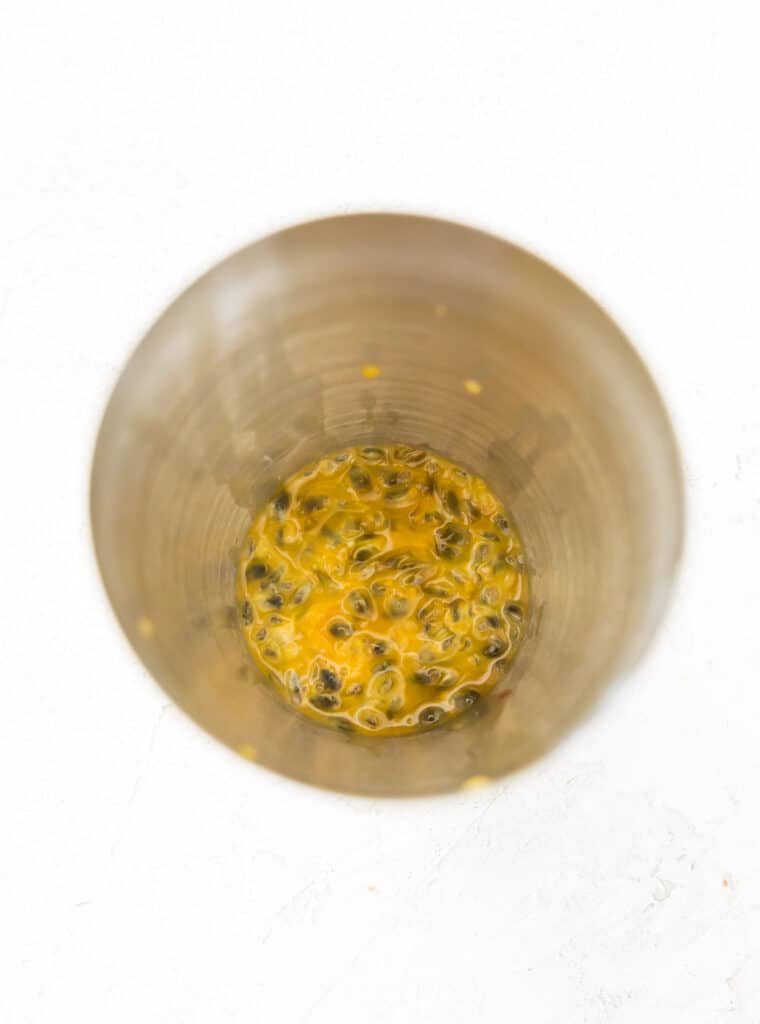 A cocktail shaker with passion fruit juice and seeds in it.
