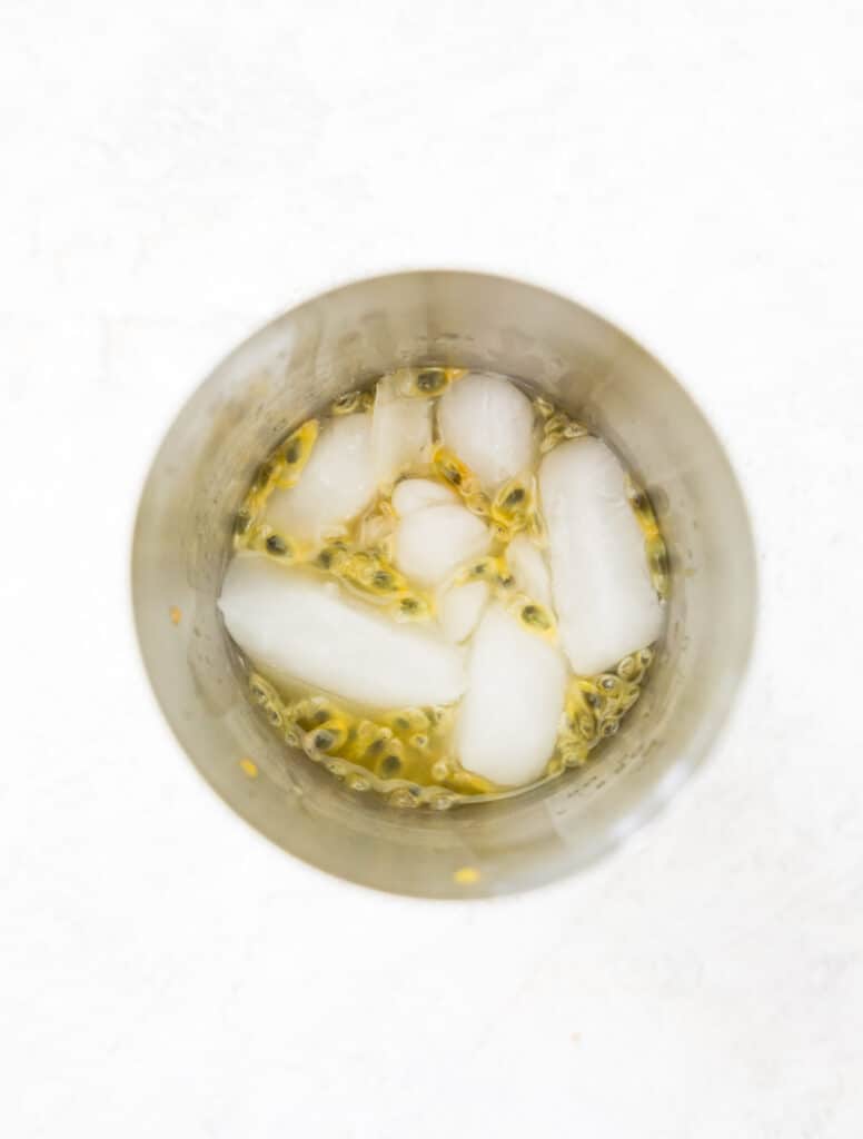 A cocktail shaker with passion fruit juice, seeds and ice cubes in it.