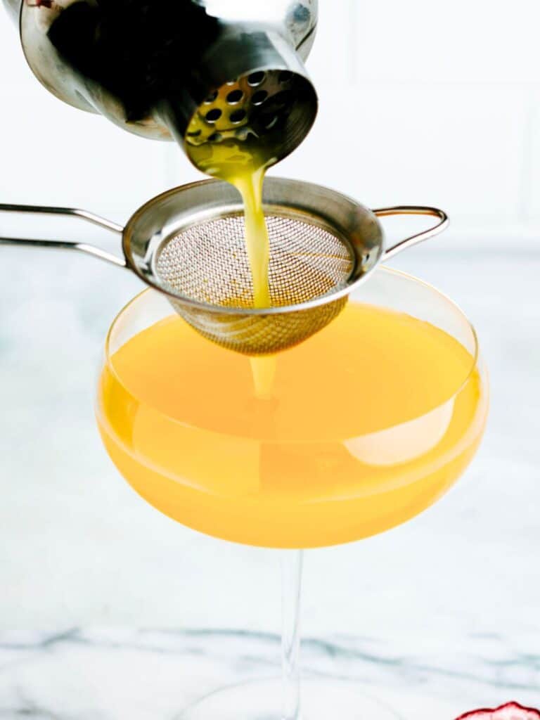 Passionfruit juice being poured from a cocktail shaker into a martini glass.