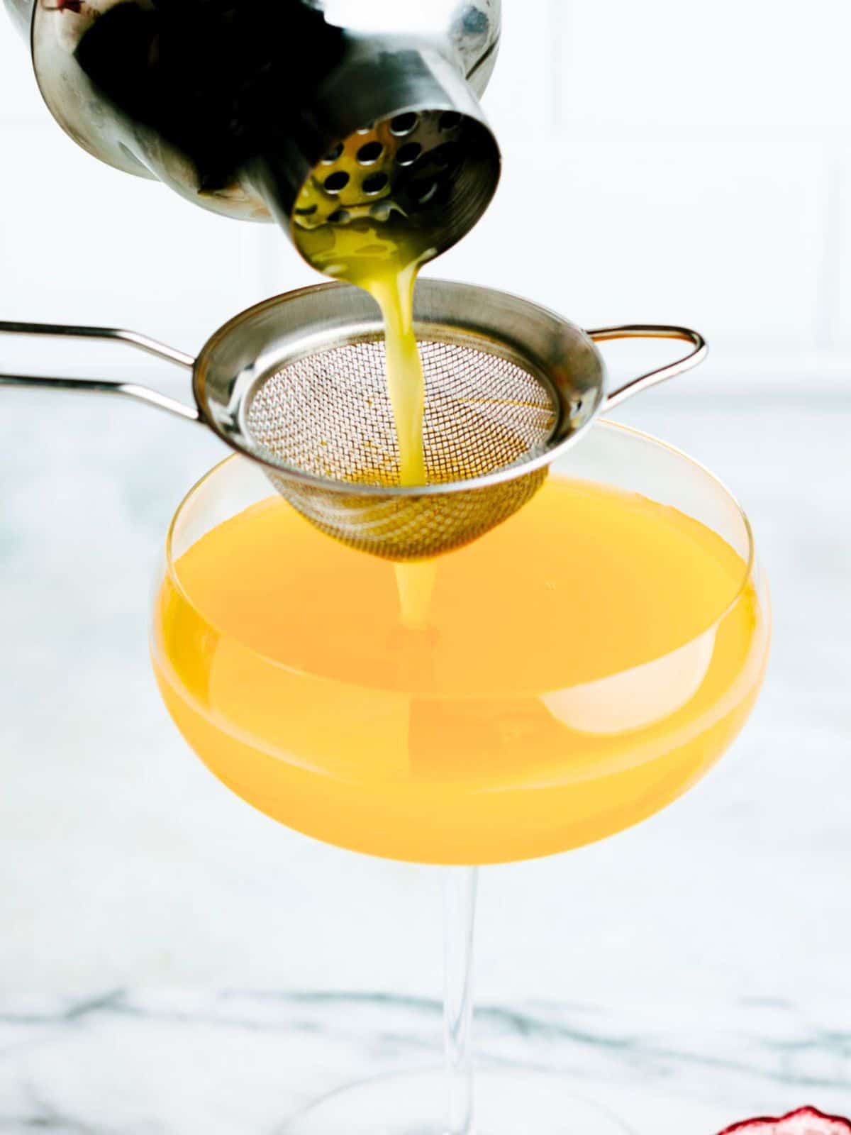A passion fruit martini being poured from a cocktail shaker into a martini glass.