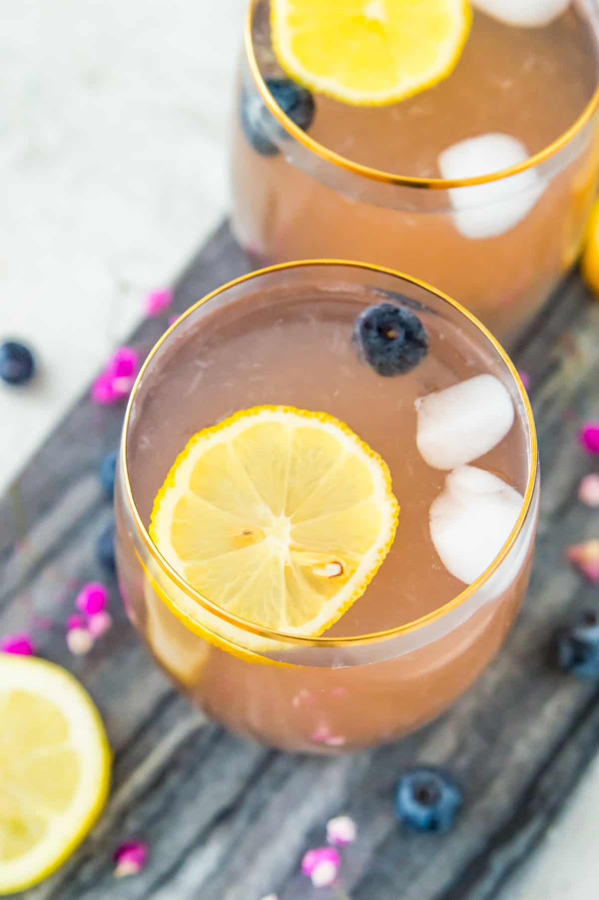 A glass of huckleberry lemonade topped with a slice of lemon, ice and fresh blueberries.