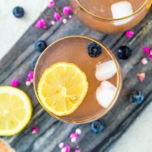 Two glasses of huckleberry lemonade topped with lemon slices and blueberries.