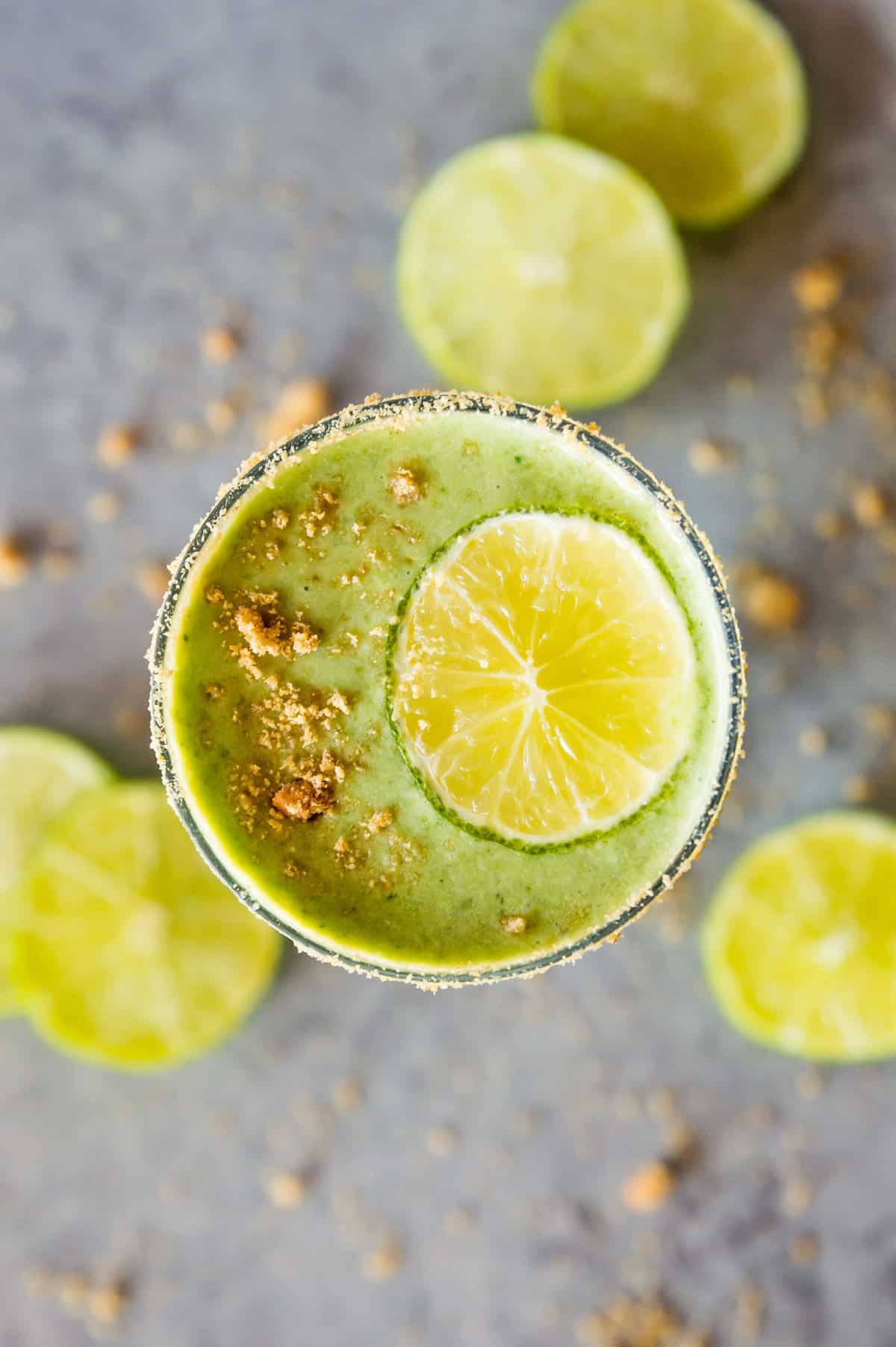A key lime pie smoothie in a glass topped with crushed graham cracker crumbs and a lime slice. 
