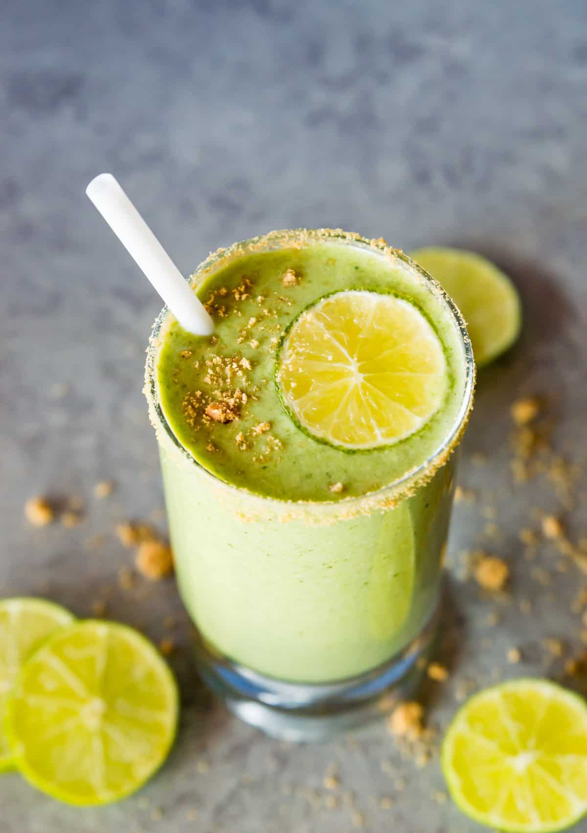 A key lime pie shake in a glass topped with a lime slice and graham cracker crumbs. 