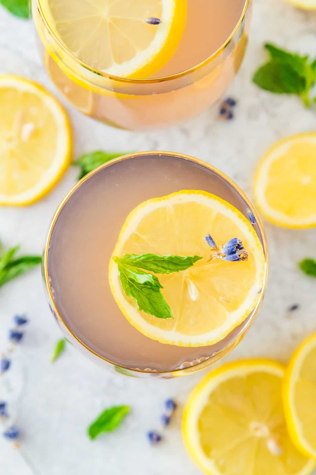 Two glasses of lemonade topped with fresh mint leaves, lemon slices and lavender flowers. 