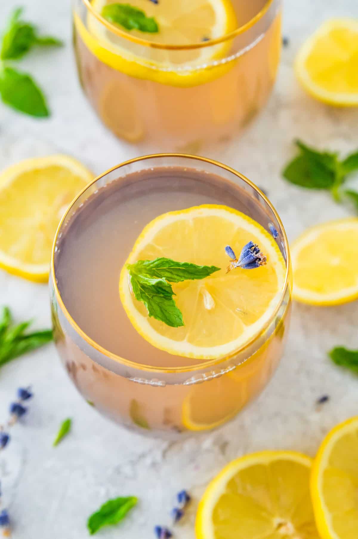 A glass of lavender mint lemonade topped with a slice of lemon, lavender flowers and mint leaves. 