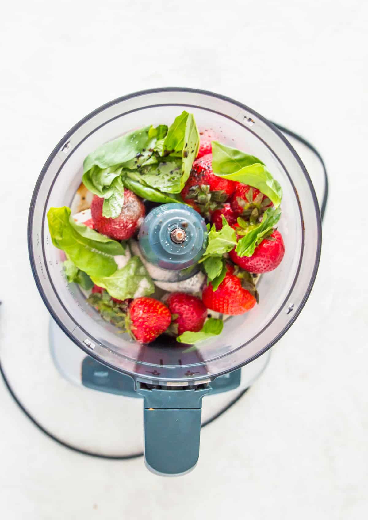 A food processor with fresh strawberries, basil leaves and salt in it.