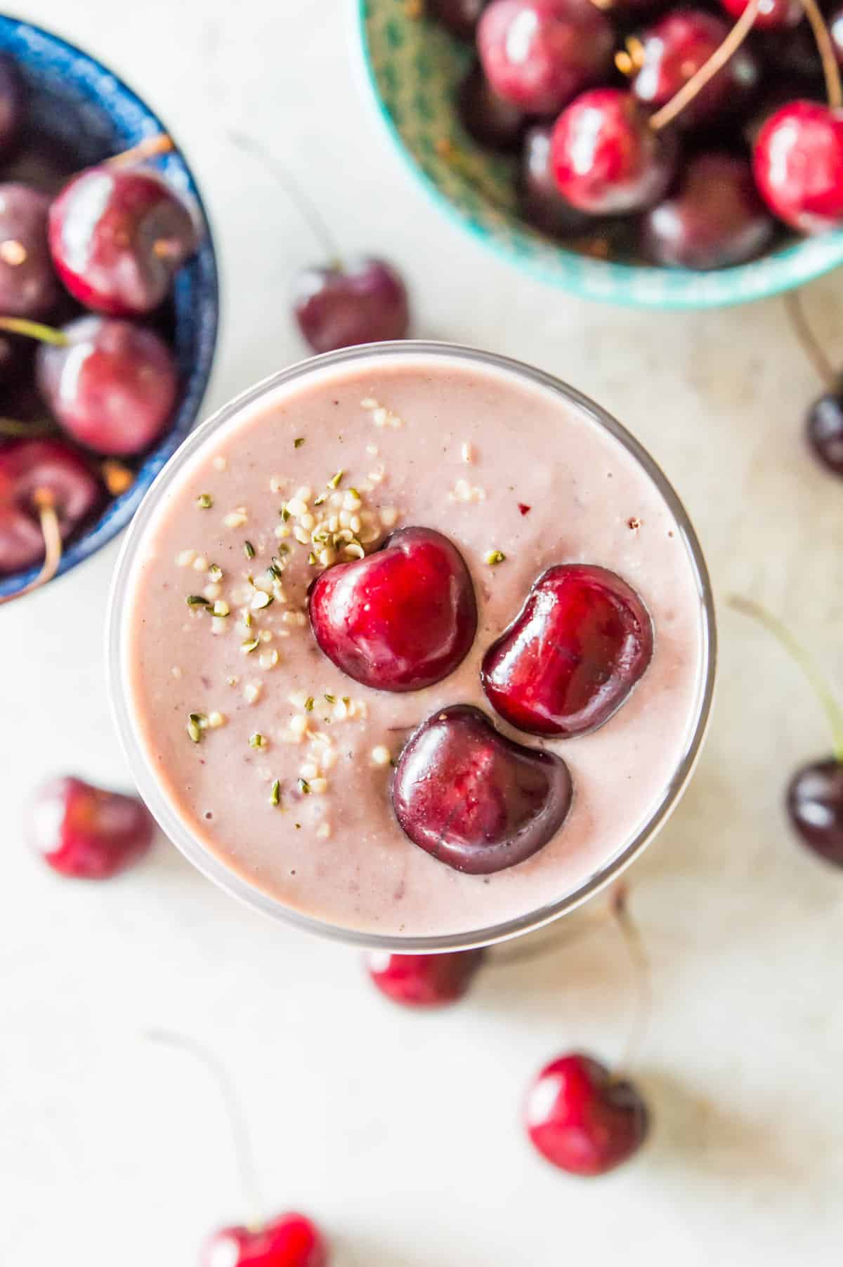 A glass filled with a cherry cheesecake smoothie topped with fresh cherries and hemp hearts.