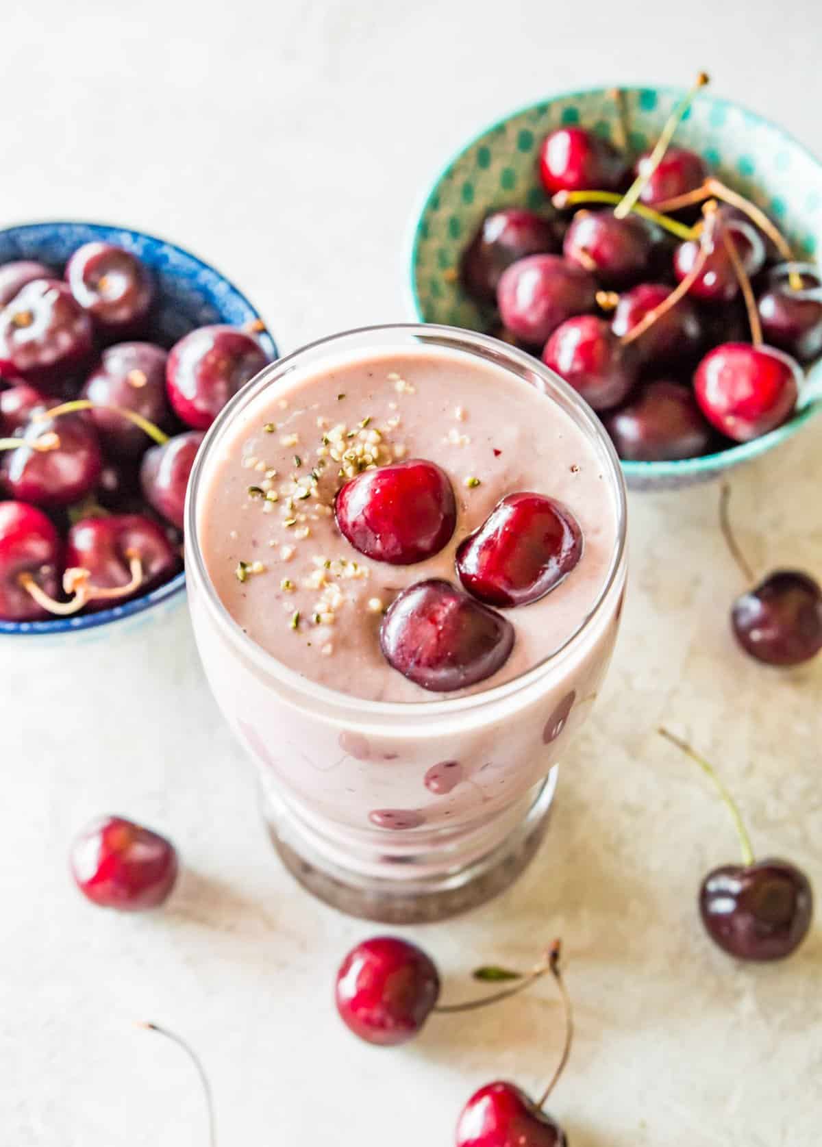 A glass filled with a cherry cheesecake smoothie topped with fresh cherries and hemp hearts.