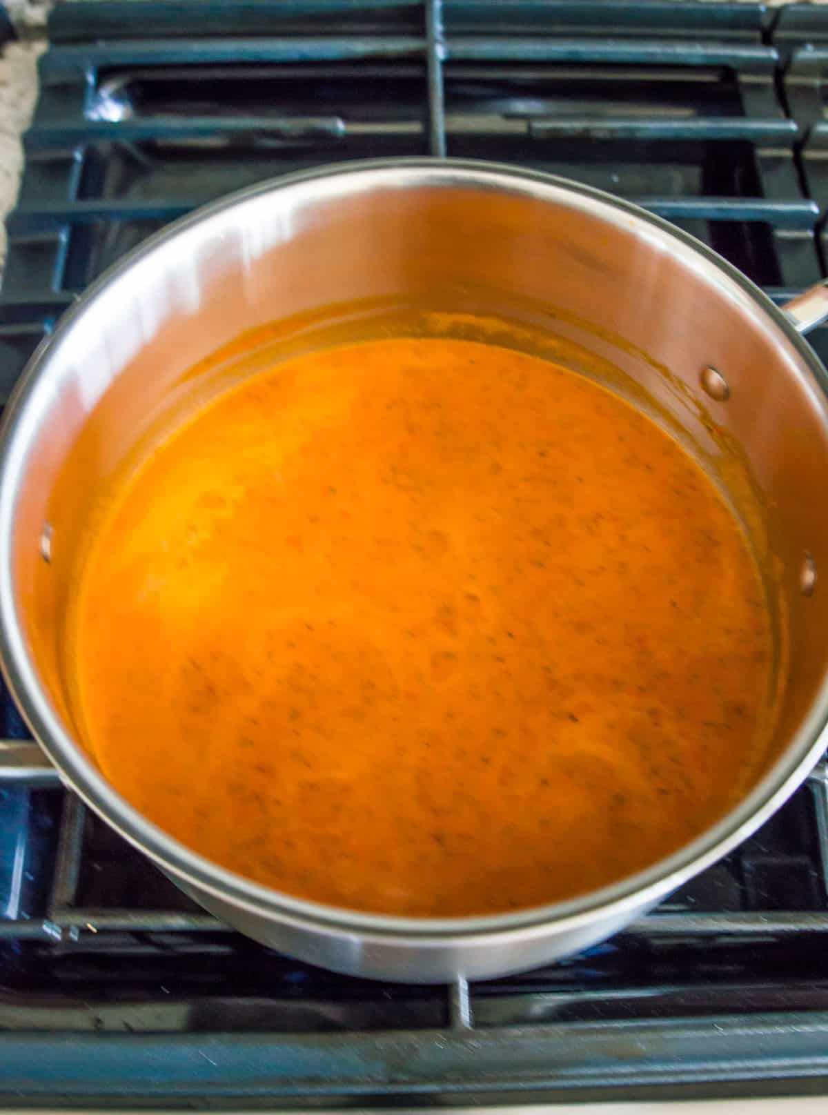 A tomato soup boiling in a pot on the stovetop.