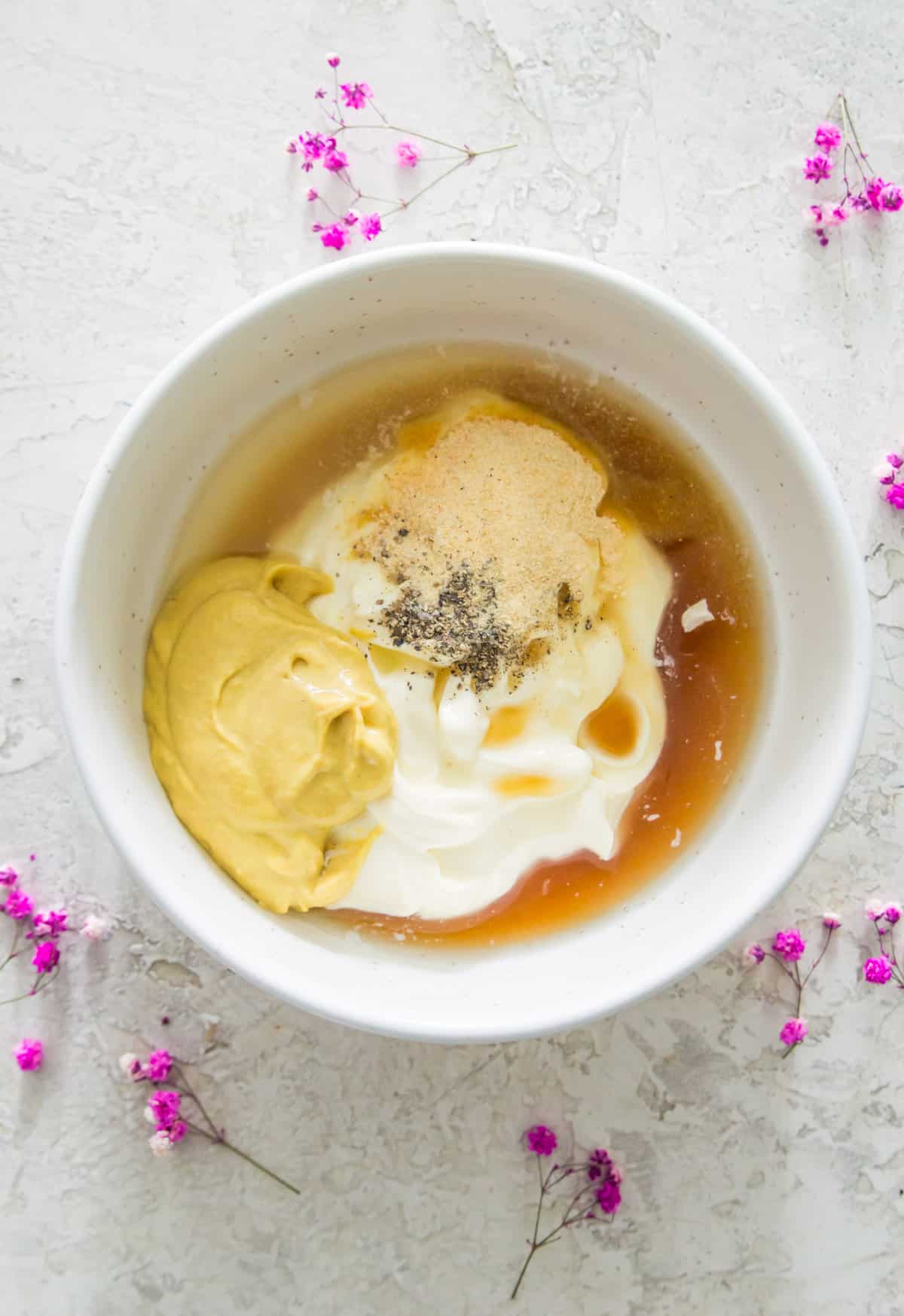 A white bowl with mayonnaise, mustard, lemon juice and spices in it.