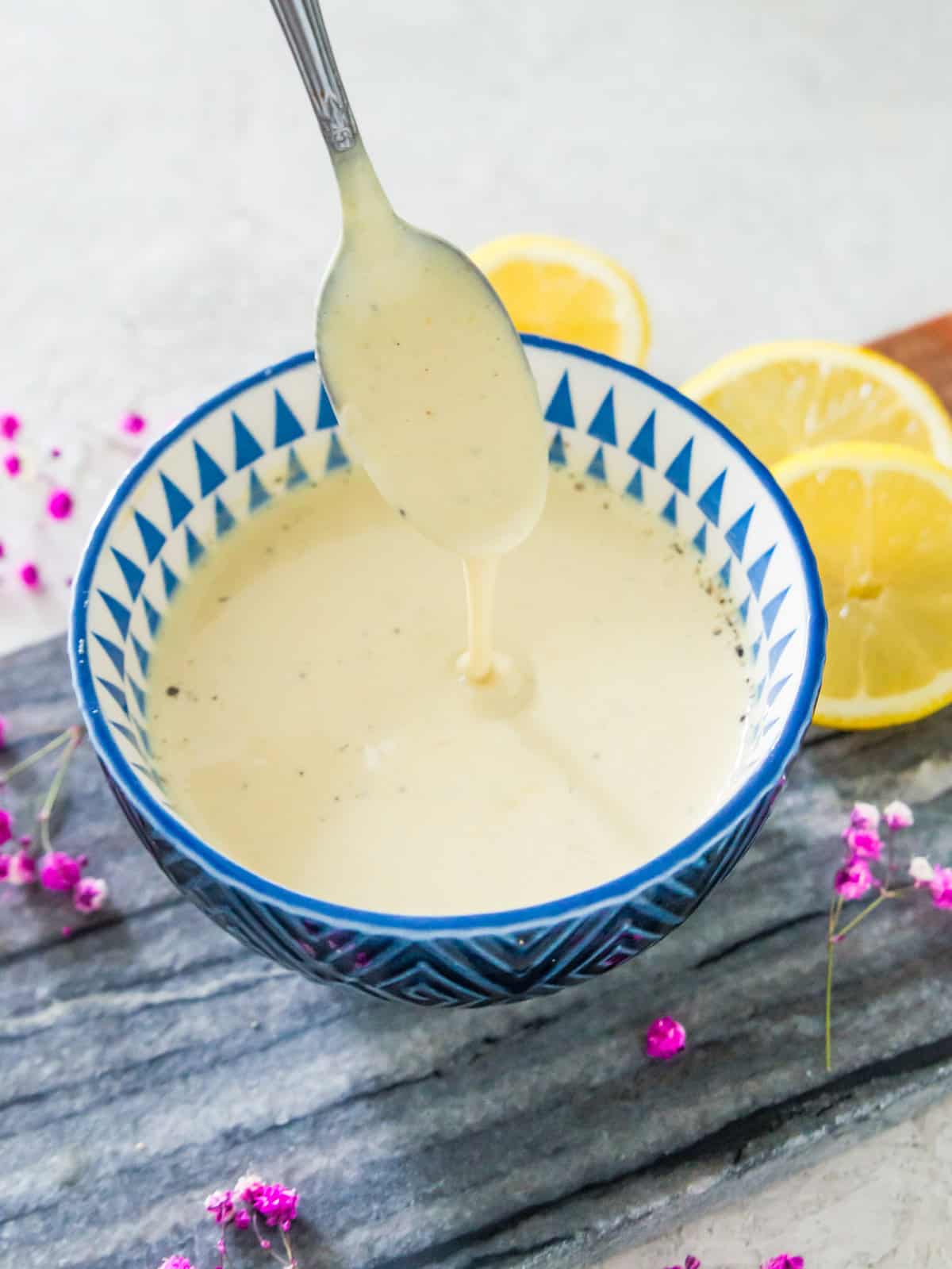 A blue bowl with mustard aioli in it and a spoon being dipped into it.