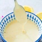 A bowl with mustard aioli in it and a spoon being dipped into it.