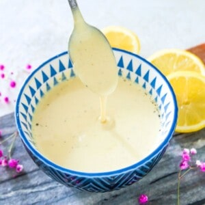 A bowl of mustard aioli with a spoon being dipped into it and lemon slices around the bowl.