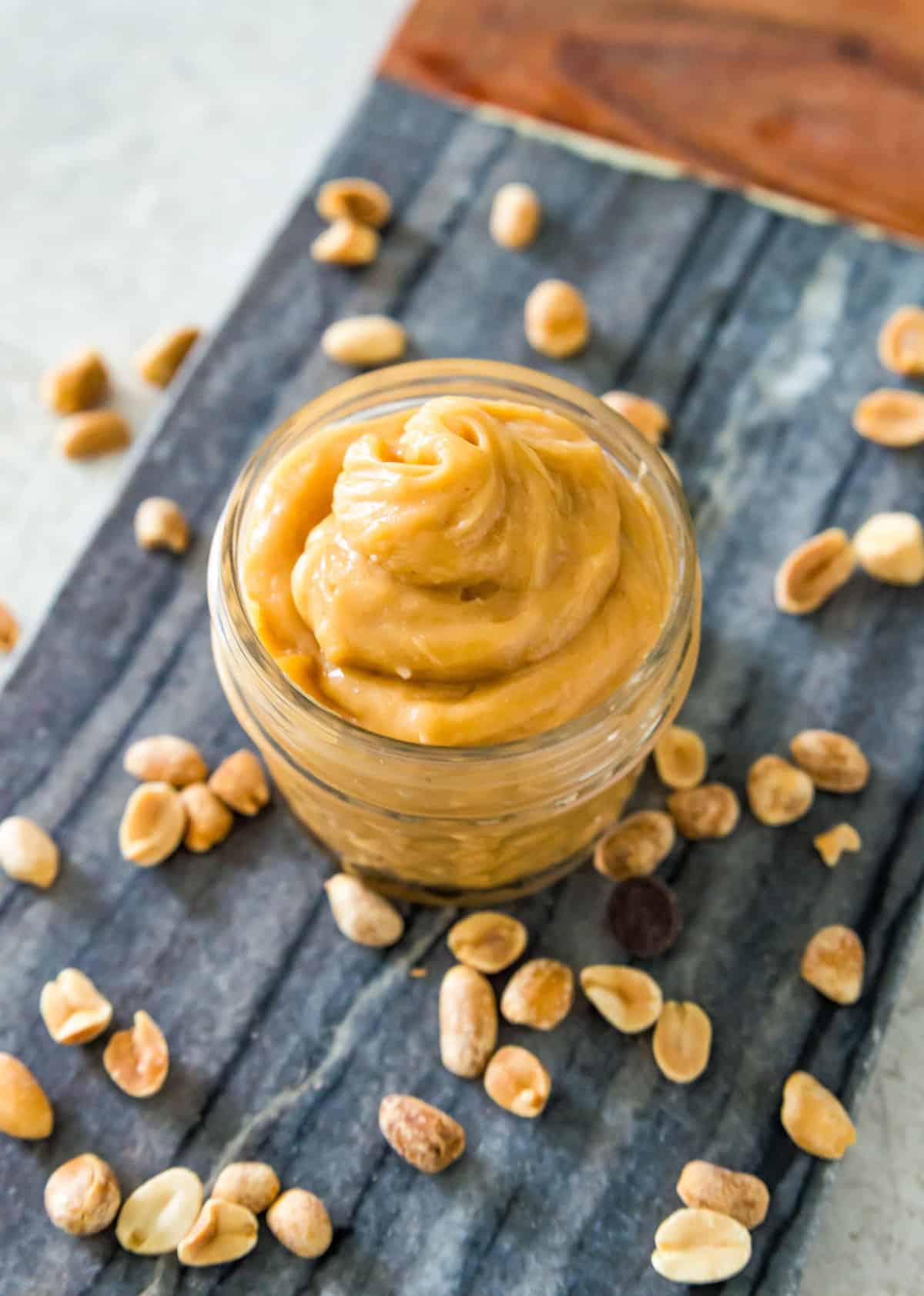 A small clear jar filled with peanut butter mousse on a serving tray with peanuts around it.