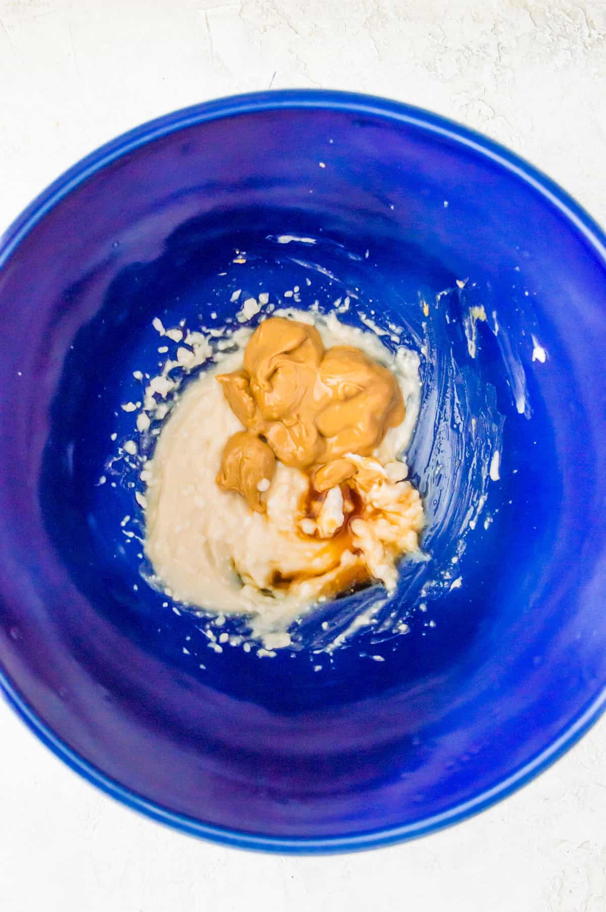 Whipped cream cheese in a large blue bowl topped with peanut butter and vanilla extract.