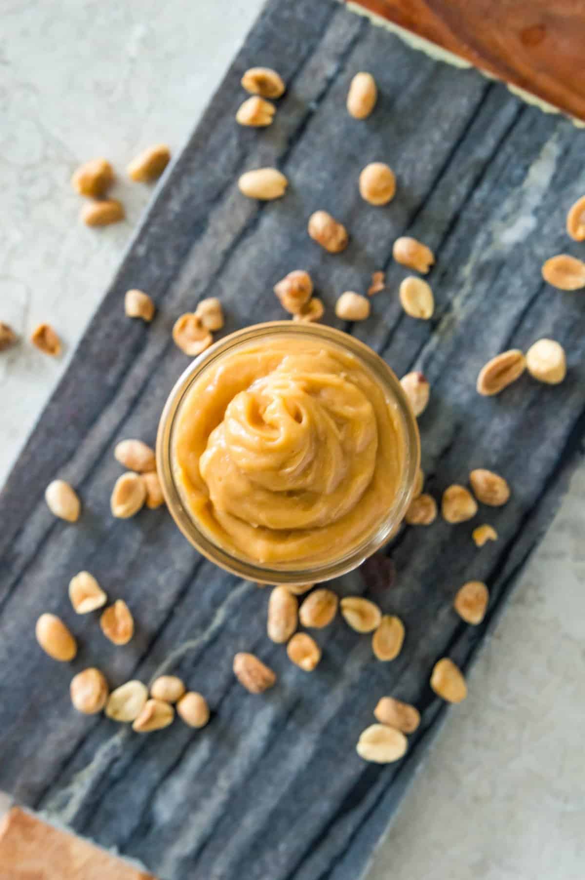 A jar filled with peanut butter mousse on a serving tray surrounded by peanuts.