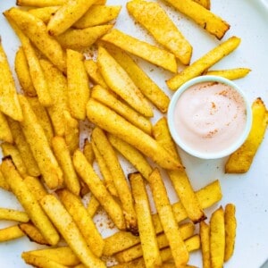 A plate of turnip fries with a small bowl of aioli next to it.