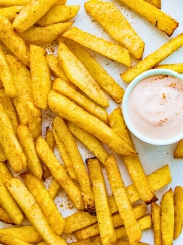 A plate of turnip fries with a small bowl of aioli next to it.