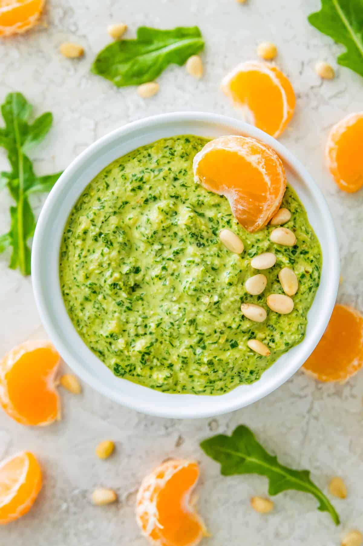 A white bowl filled with pesto and garnished with pine nuts and an orange slice. 
