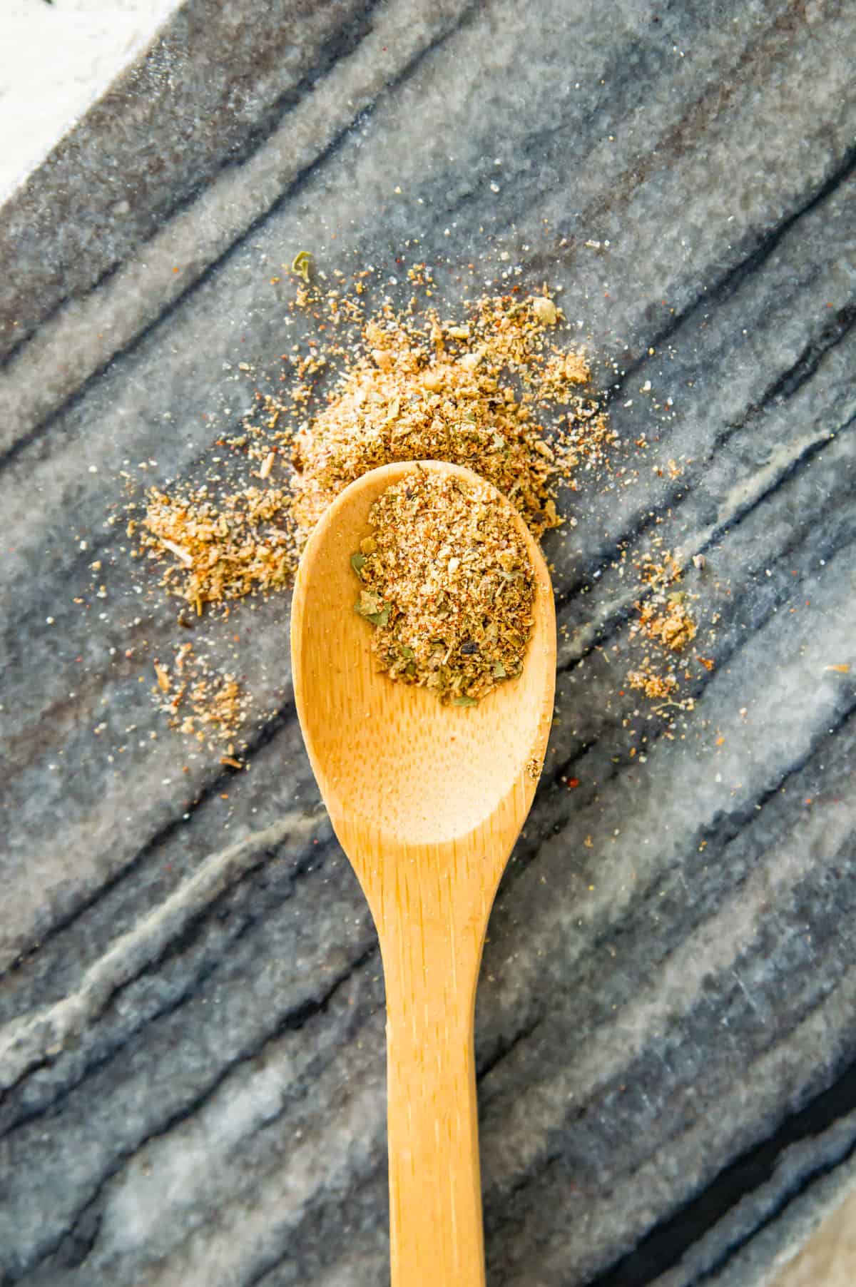 A wooden spoon with a spice blend spilling out of it.