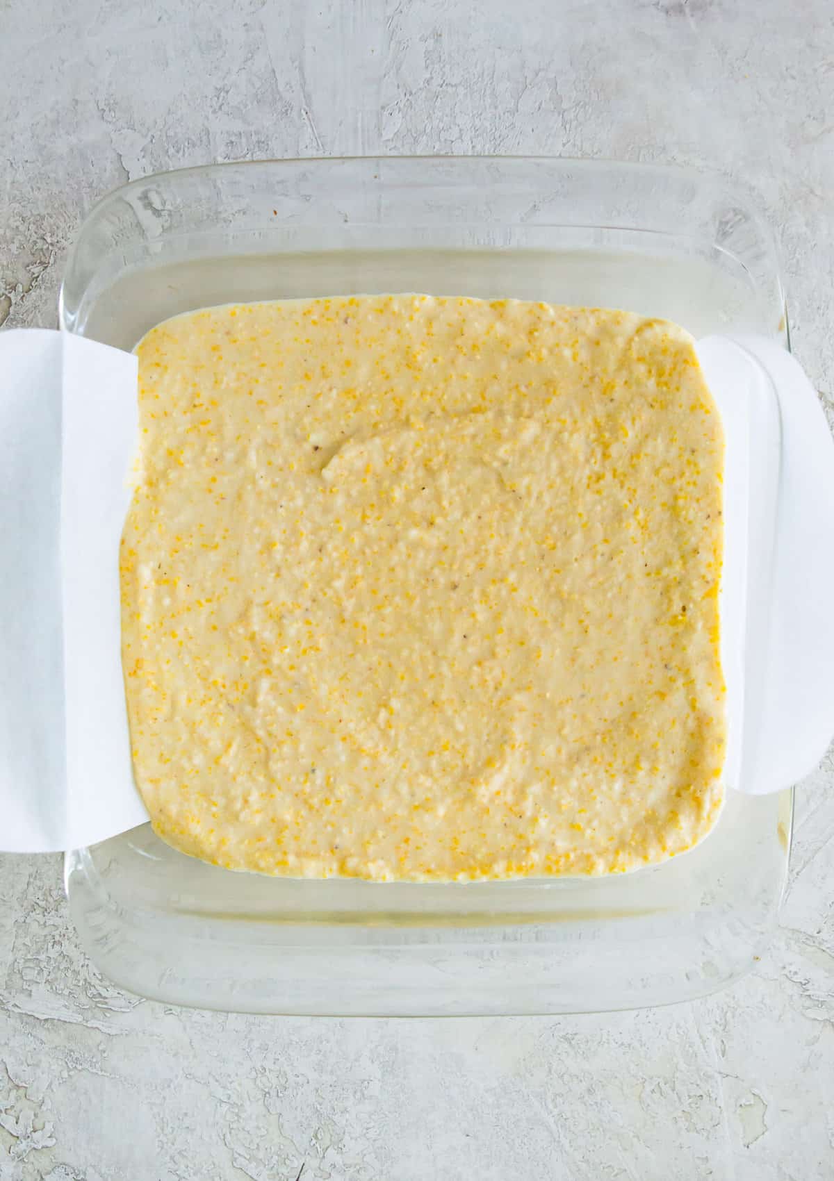 A square glass baking dish with the batter for making cornbread in it.