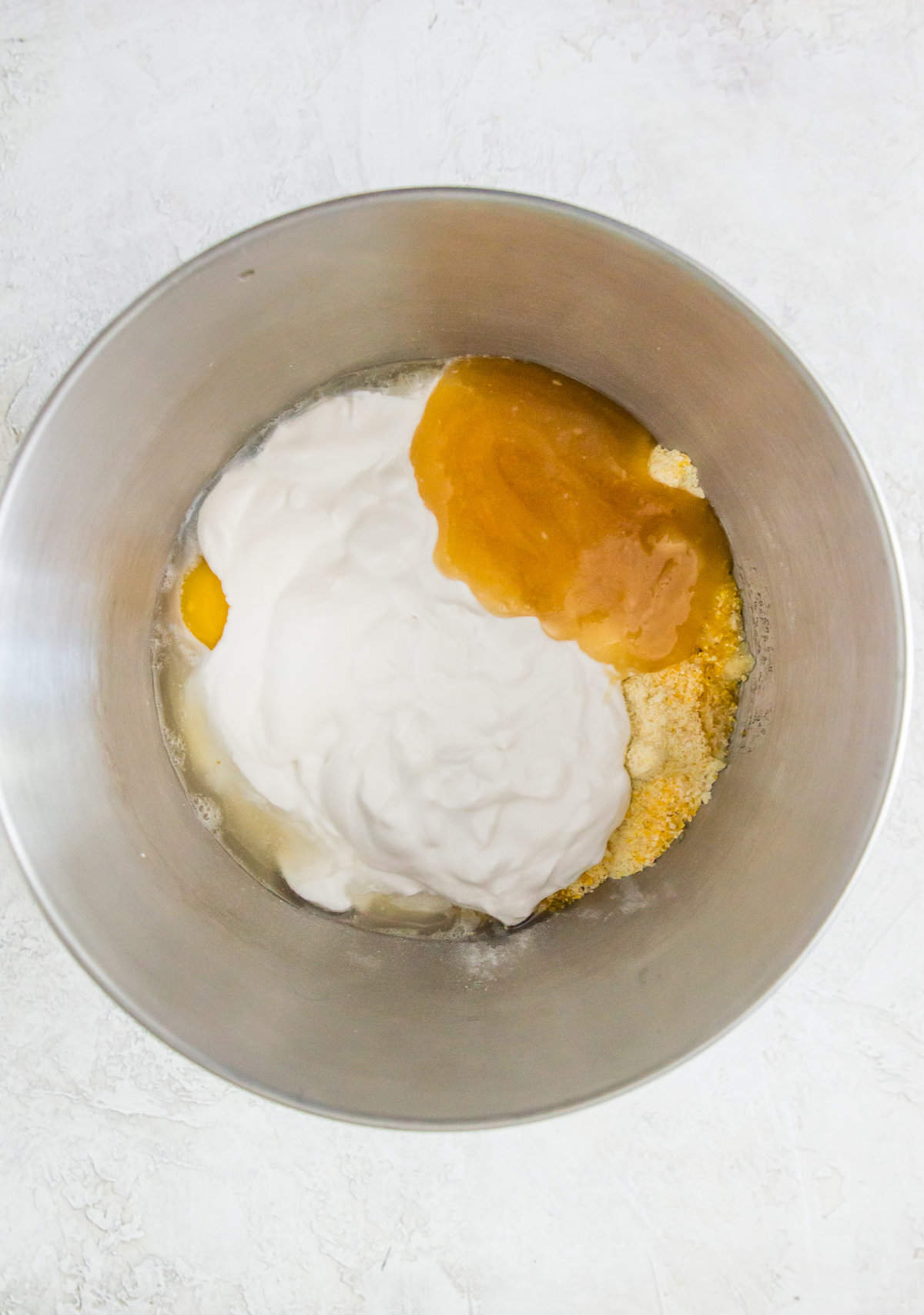 A large bowl with yogurt, honey, an egg, cornmeal and almond flour in it.