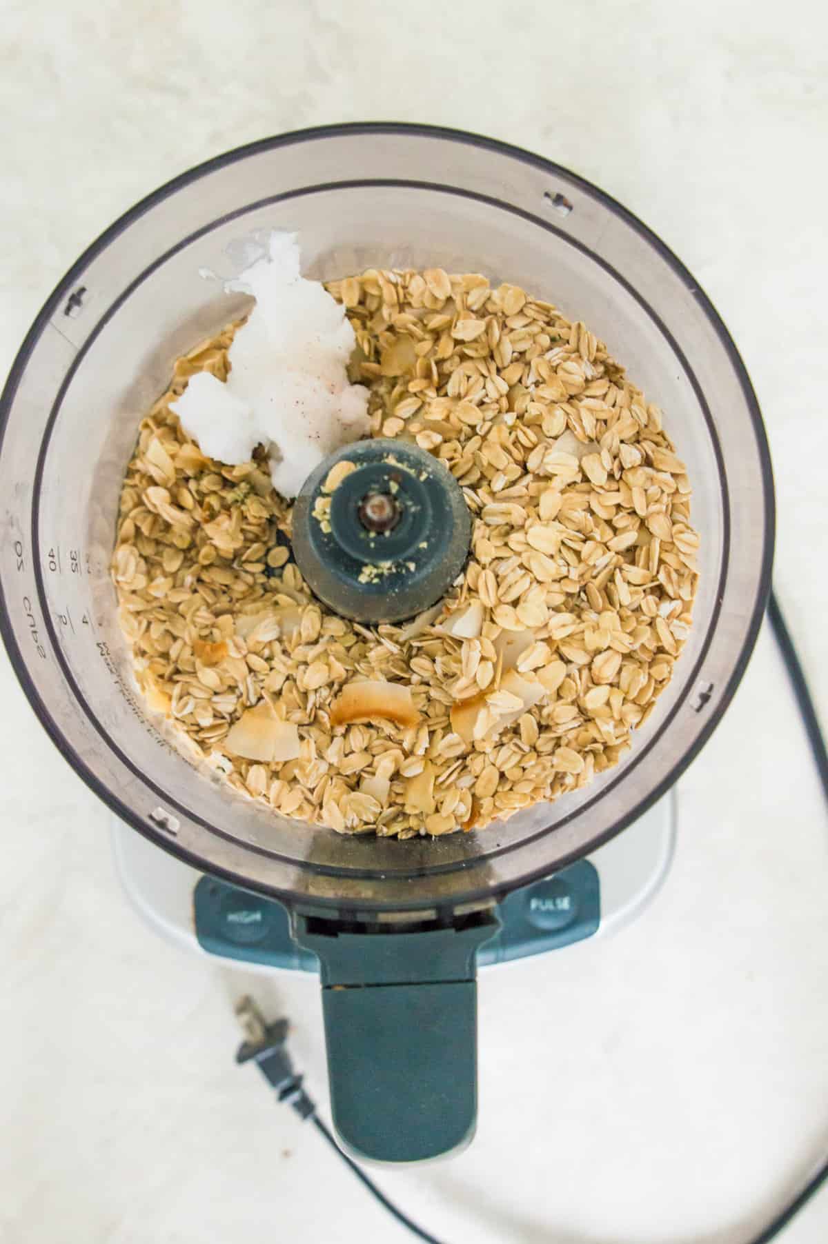 A food processor filled with oats, coconut oil and coconut flakes. 