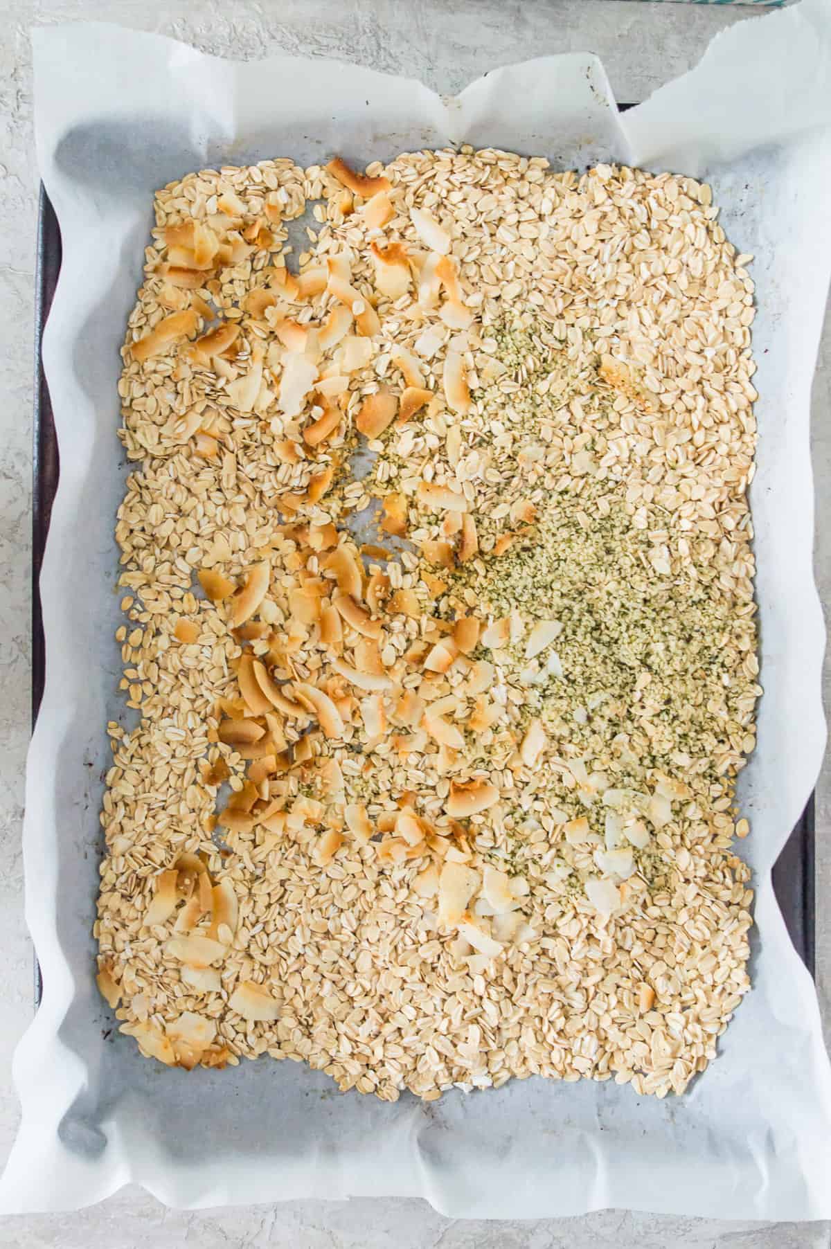 Toasted oats and coconut flakes pn a baking sheet lined with parchment paper. 